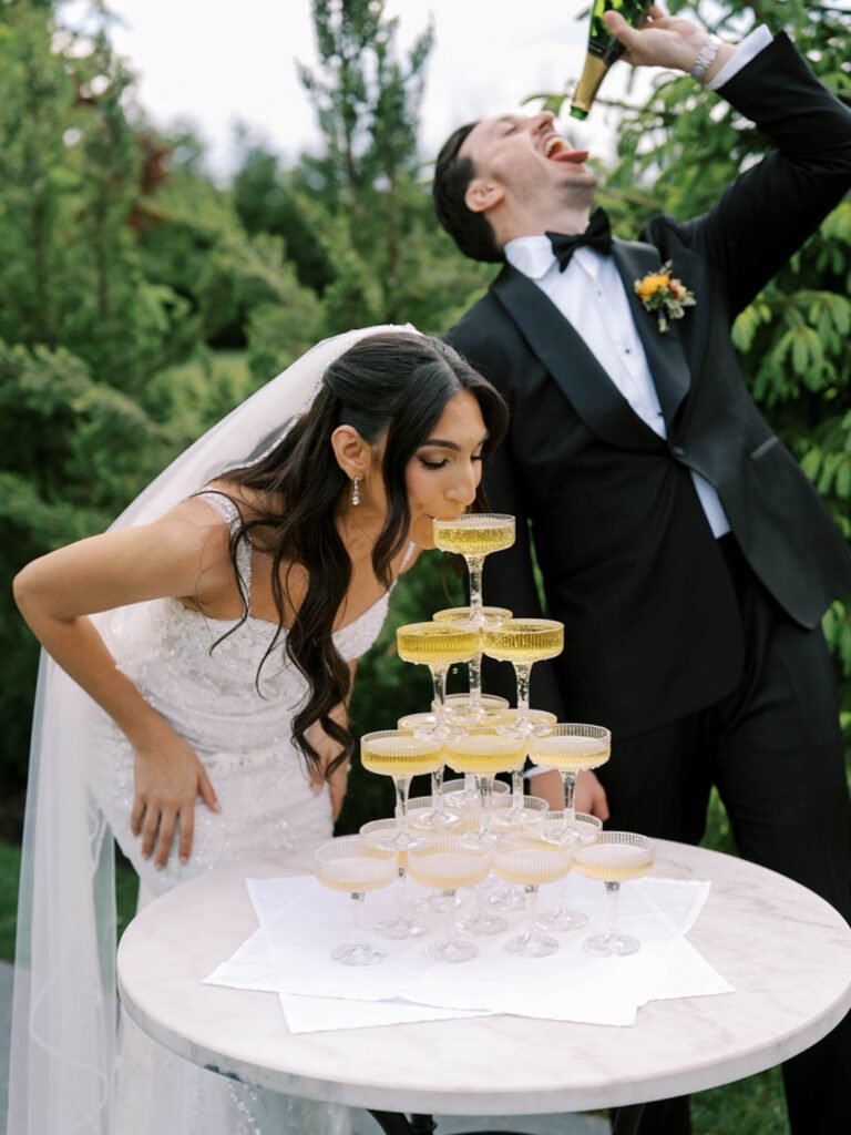 Groom pours champagne over a champagne tower as the bride leans in