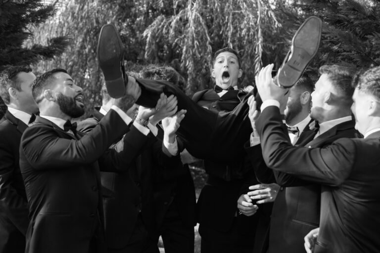 Black-and-white photo of groomsmen hoisting the groom in celebration