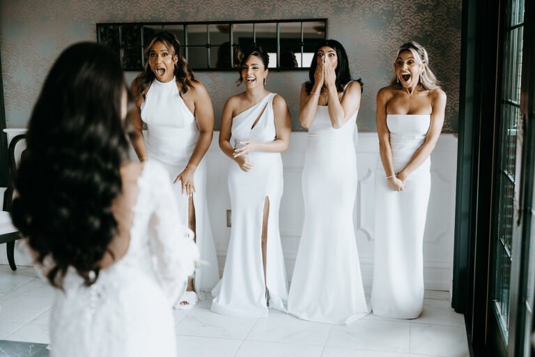 Bridesmaids in white react to seeing the bride for the first time