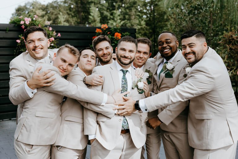 Groom embraced by groomsmen in tan suits in the garden