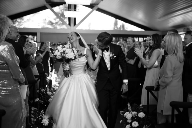 Black-and-white photo of guests cheering as the newlyweds walk back up the aisle