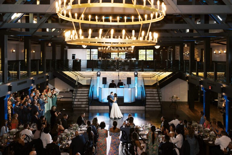 Couple's first dance beneath candlelit ring chandeliers as guests look on in the Park Loft dance hall