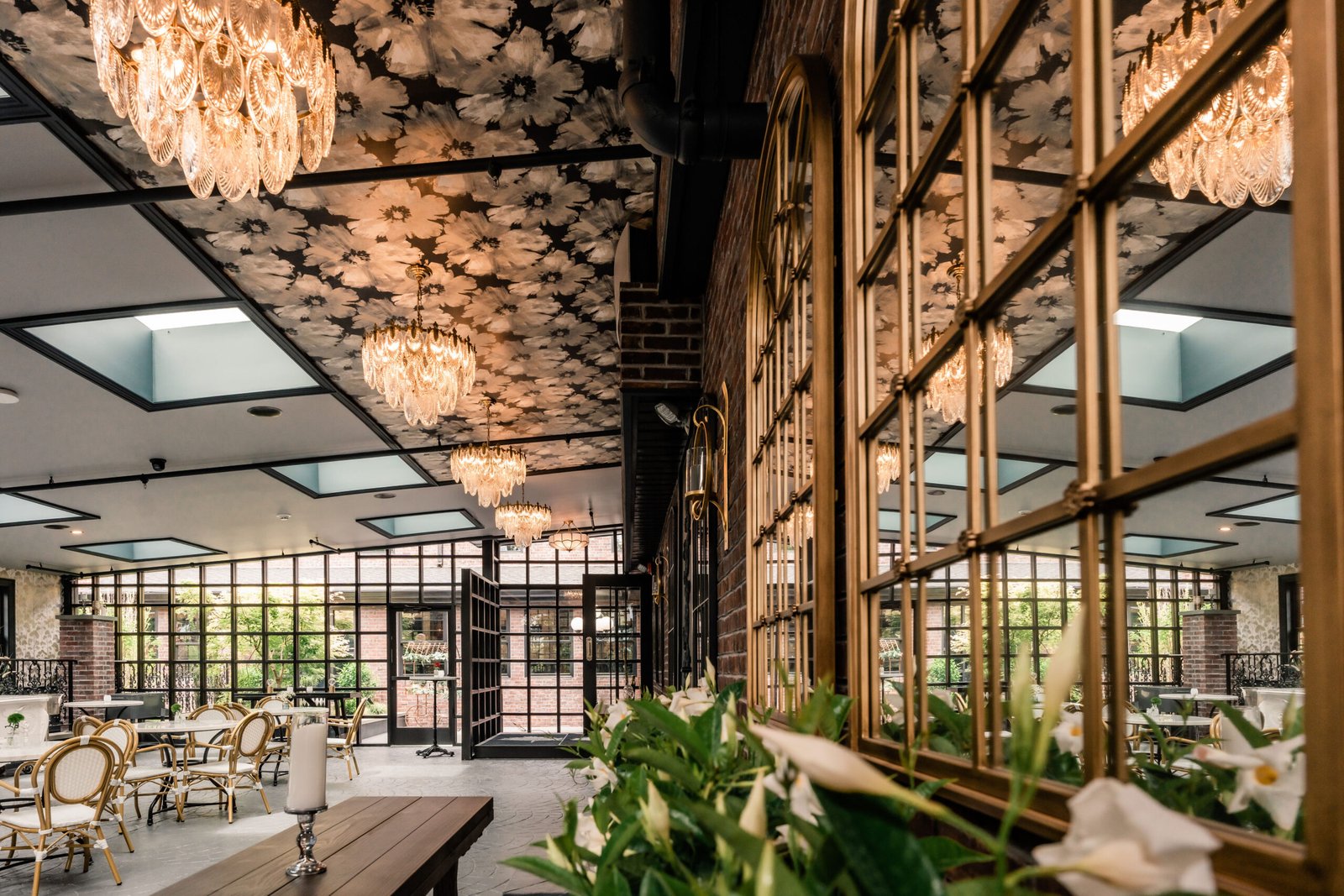 Glass-walled atrium at Park Loft with a floral ceiling installation, crystal chandeliers and bistro seating