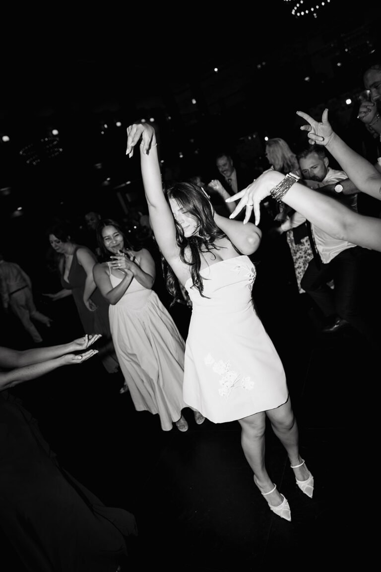 Black-and-white photo of the bride dancing with guests in a short reception dress