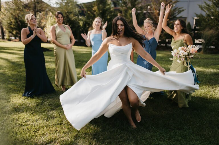Bride twirls her gown on the lawn as bridesmaids cheer behind her
