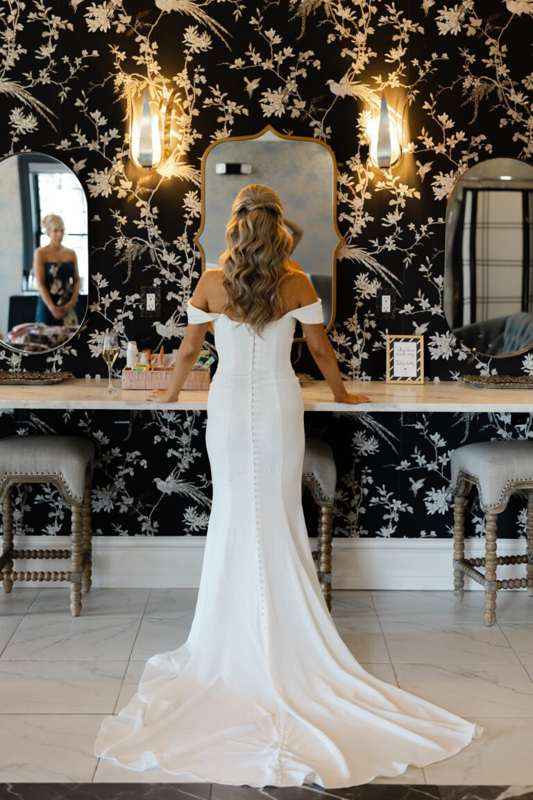 Bride stands at the vanity in the Park Loft bridal suite, with dark botanical wallpaper