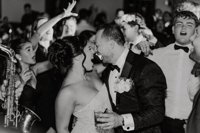 Black-and-white photo of a couple dancing with guests and a live saxophonist during the reception