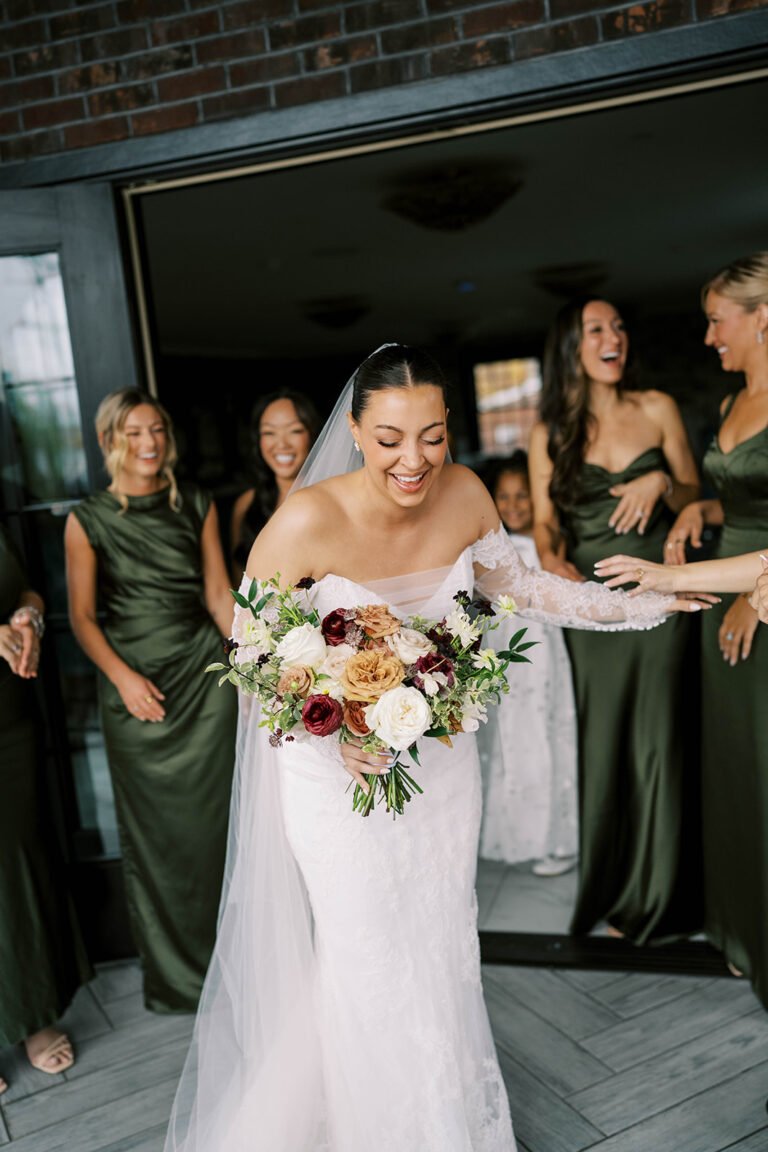 Bride with a colorful bouquet steps out as bridesmaids in olive green cheer behind her