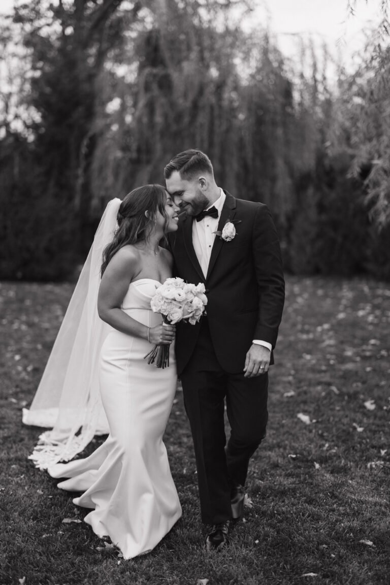 Black-and-white photo of a bride and groom walking together on the lawn