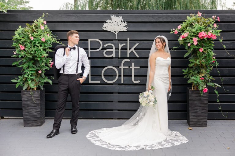 Bride and groom pose in front of the Park Loft wall sign flanked by flowering planters