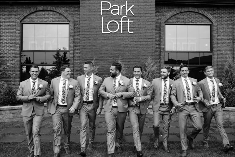 Black-and-white photo of groomsmen in suspenders walking in front of the Park Loft building