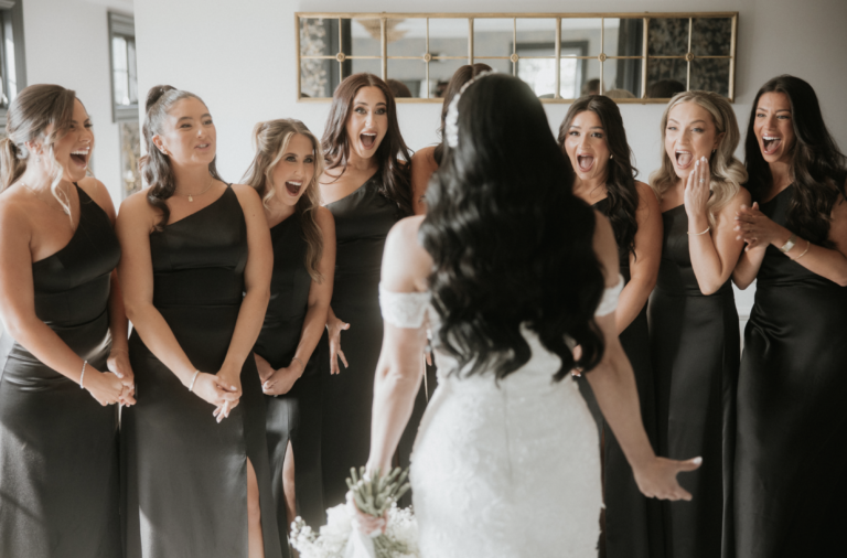 Bridesmaids in black gowns react as the bride turns to face them