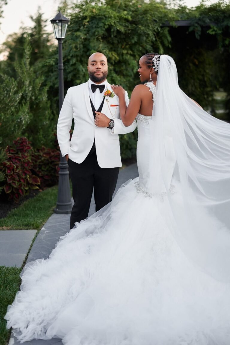 Groom in a white dinner jacket with the bride, her cathedral veil flowing, on the patio