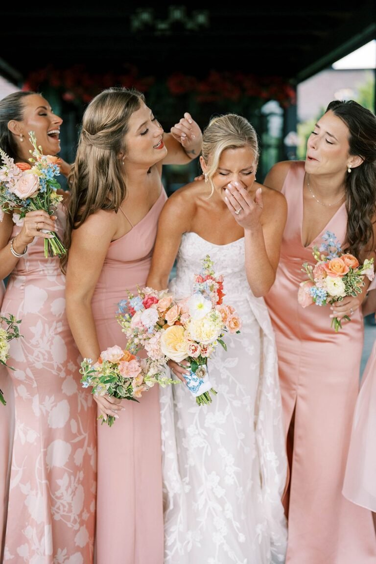 Bride laughs with bridesmaids in blush pink dresses holding pastel bouquets