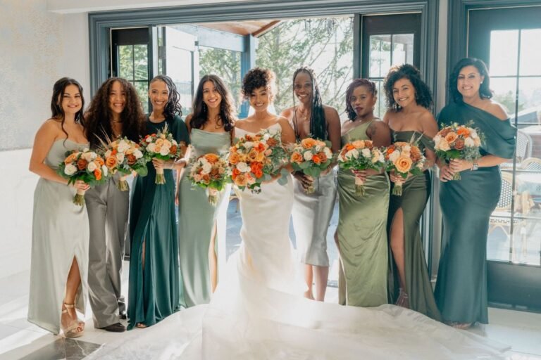 Bride with bridesmaids in sage and emerald gowns holding peach bouquets