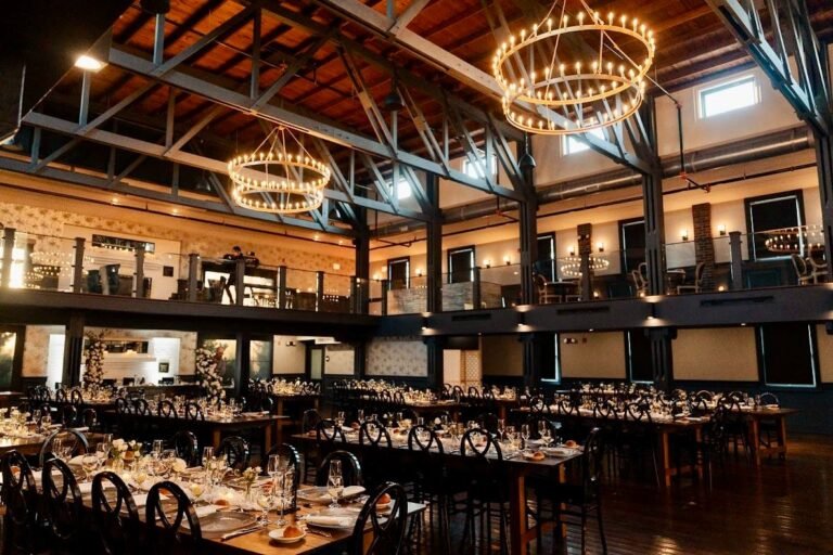 Park Loft dance hall set with long banquet tables beneath ring chandeliers and exposed wood beams