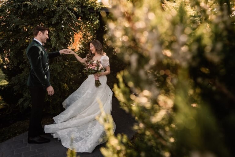 Groom twirls the bride along a garden path at dusk