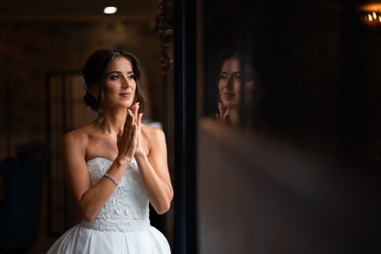 Bride clasps her hands in delight while getting ready by the window