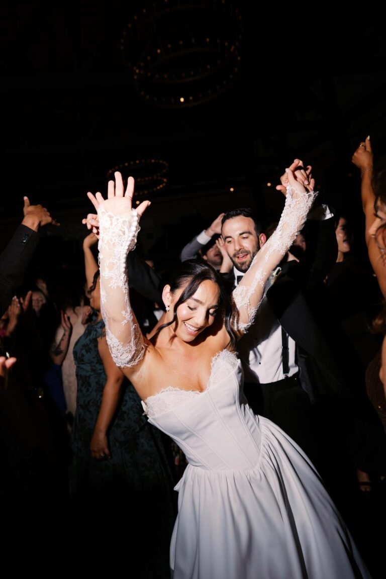 Bride throws her arms up dancing with the groom late in the reception