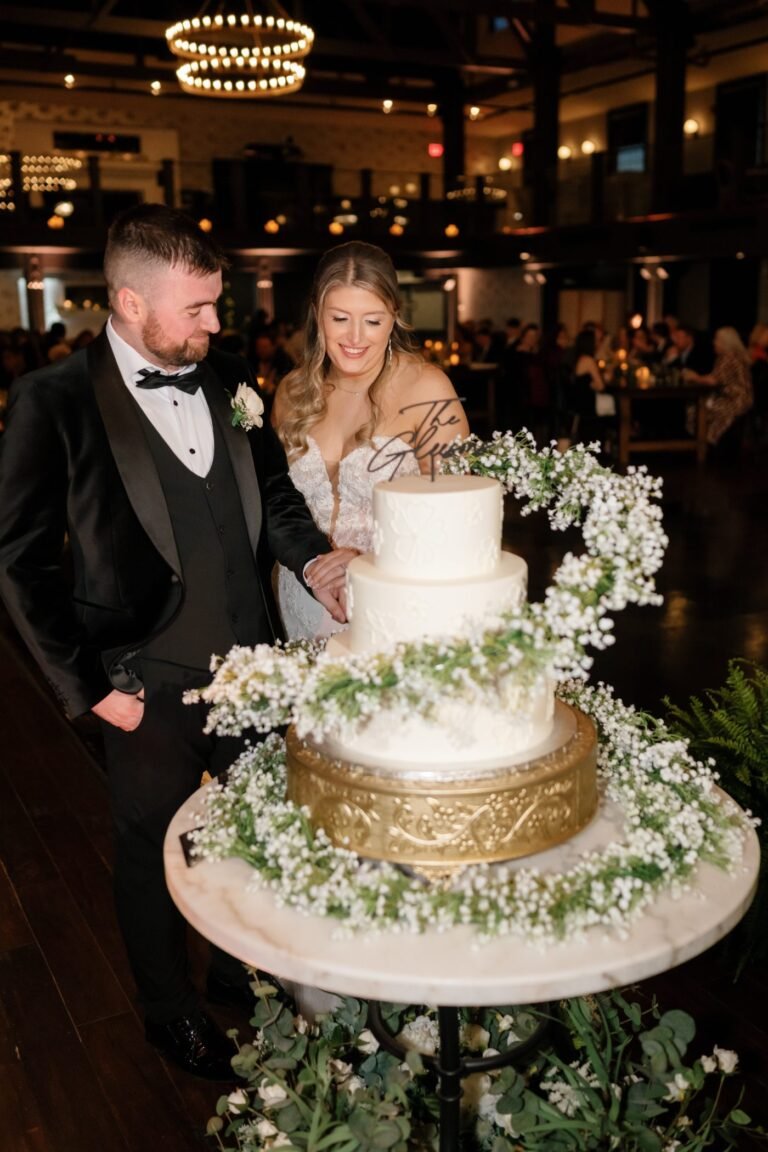 Bride and groom cut a tiered cake decorated with greenery and gold